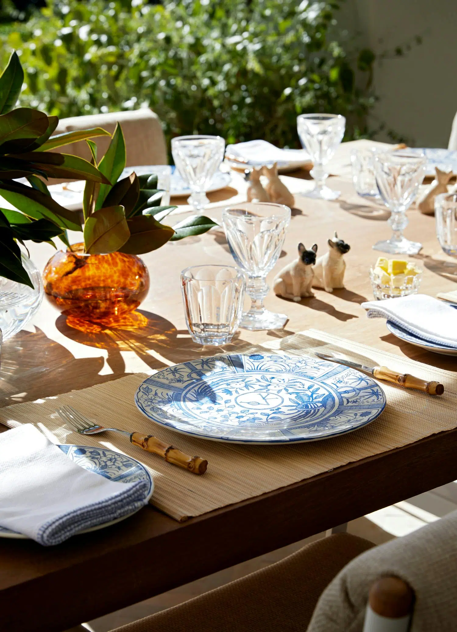 An outdoor, wooden dining table with crockery, cutlery and glassware on top.