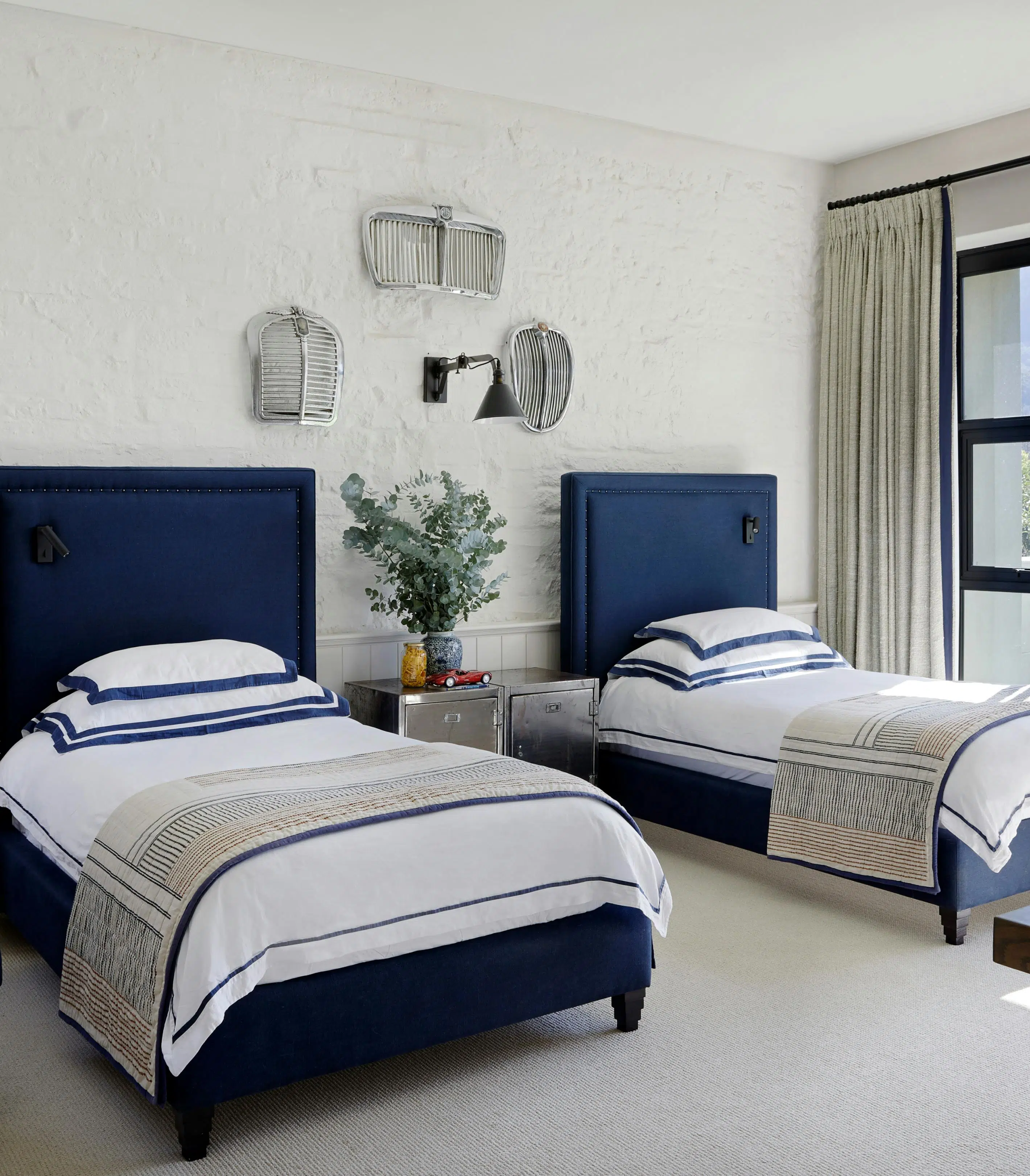 Two single beds in a dark blue tone are on either side of a mirrored bedside table.