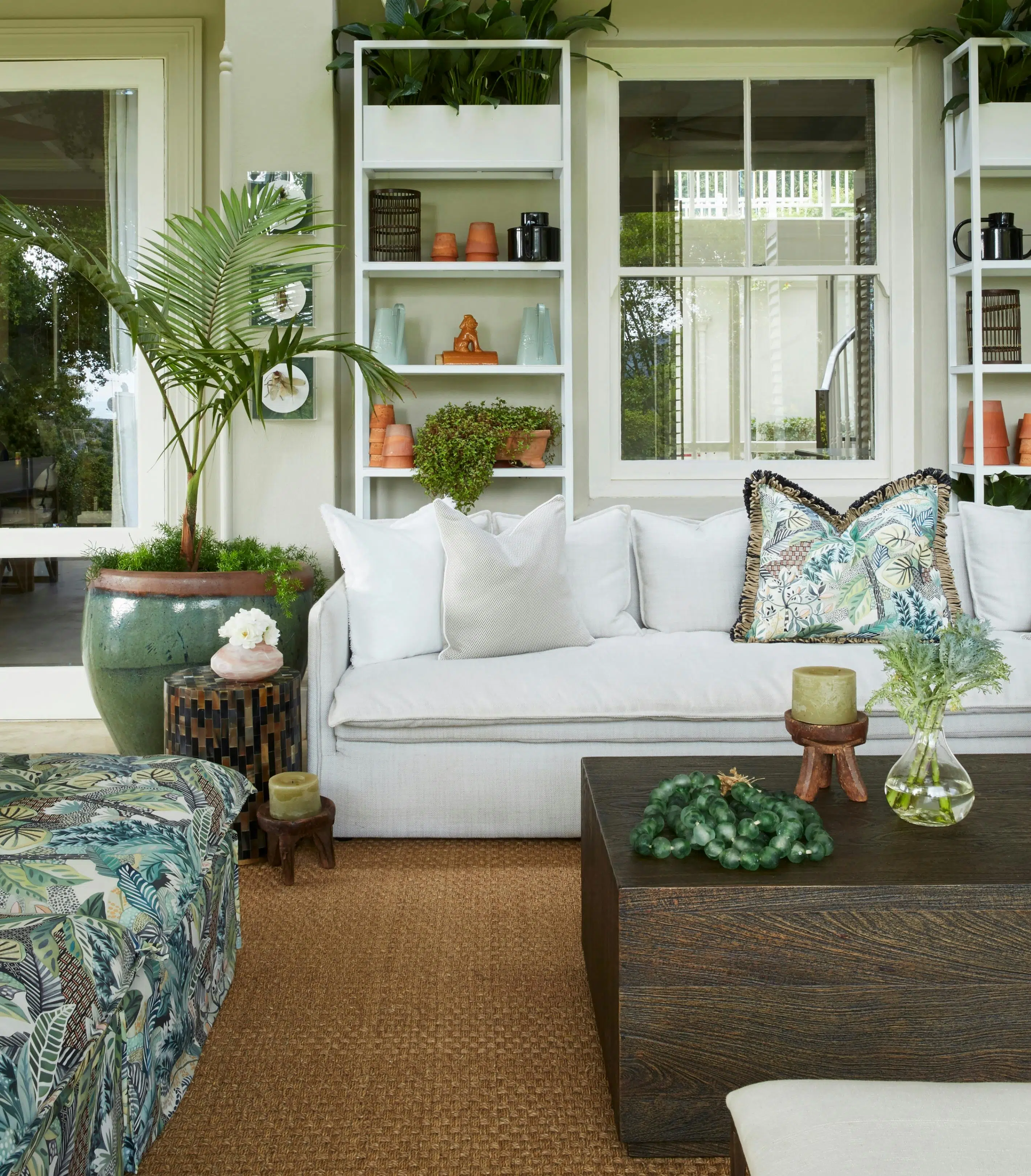 Close-up of a wooden coffee table with a white sofa in the background. Behind the sofa is a large potted plant.