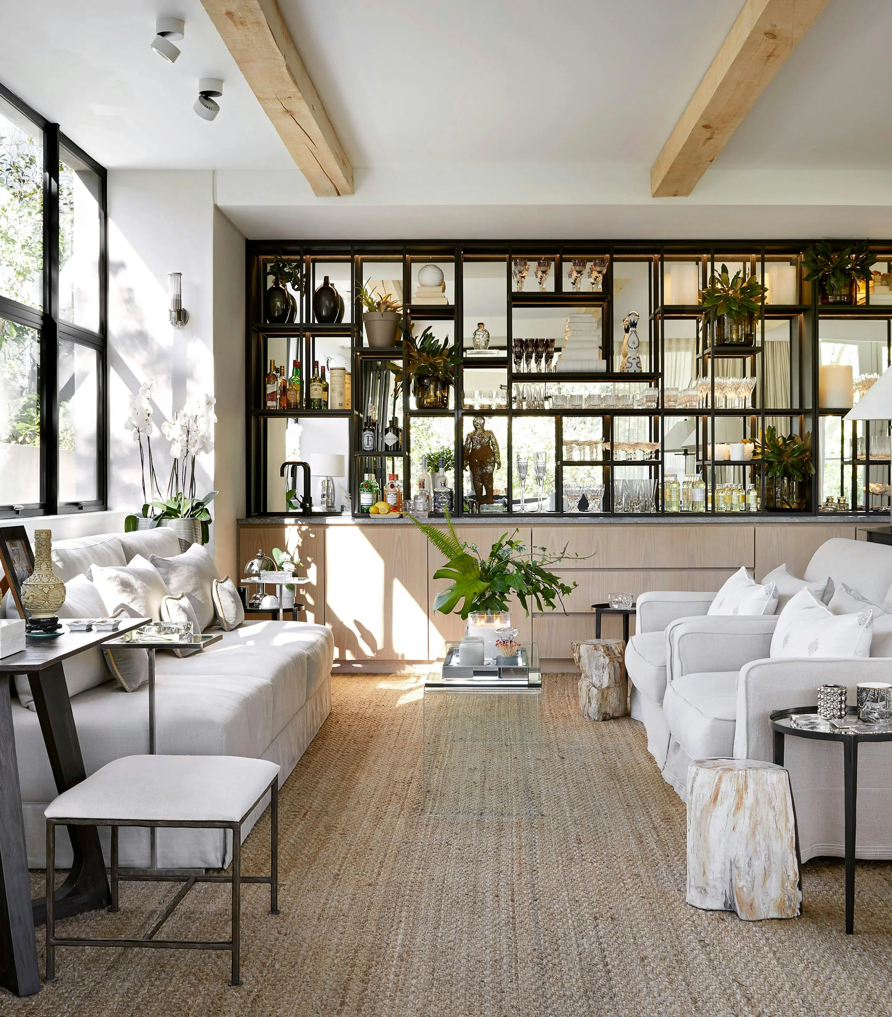 Two sofas parallel to one another with a glass coffee table in the middle. In the background, shelving that features glasses, bottles of alcohol and other decorative accents.