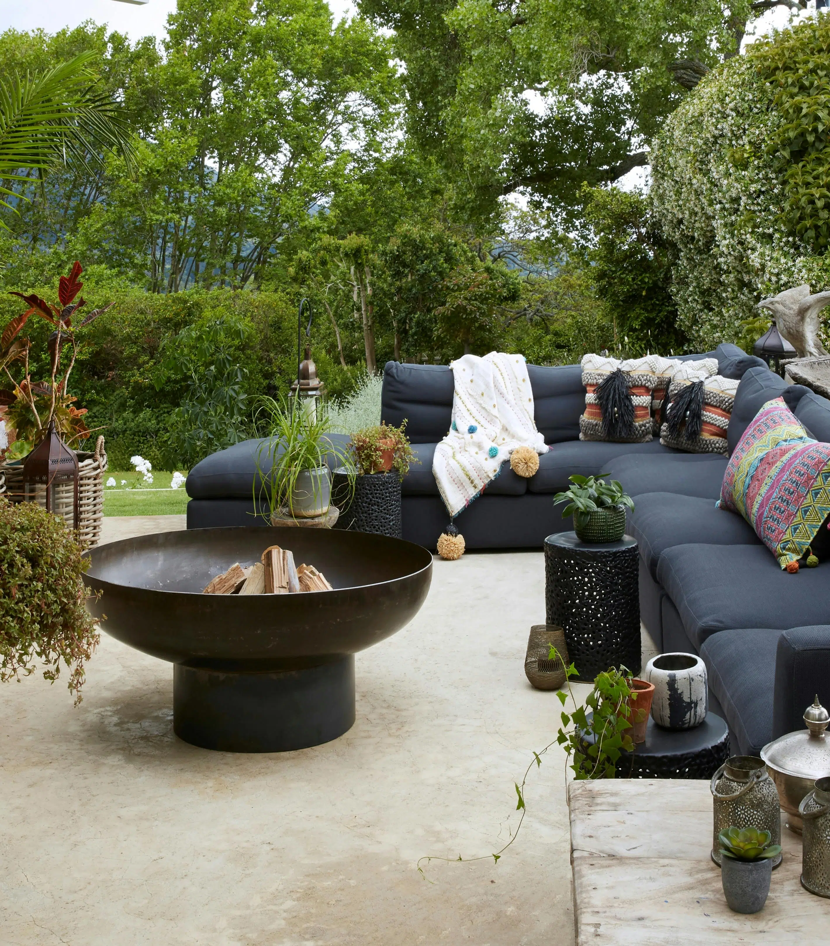 A Moroccan-inspired fire pit is surrounded by an outdoor sofa and lush greenery.