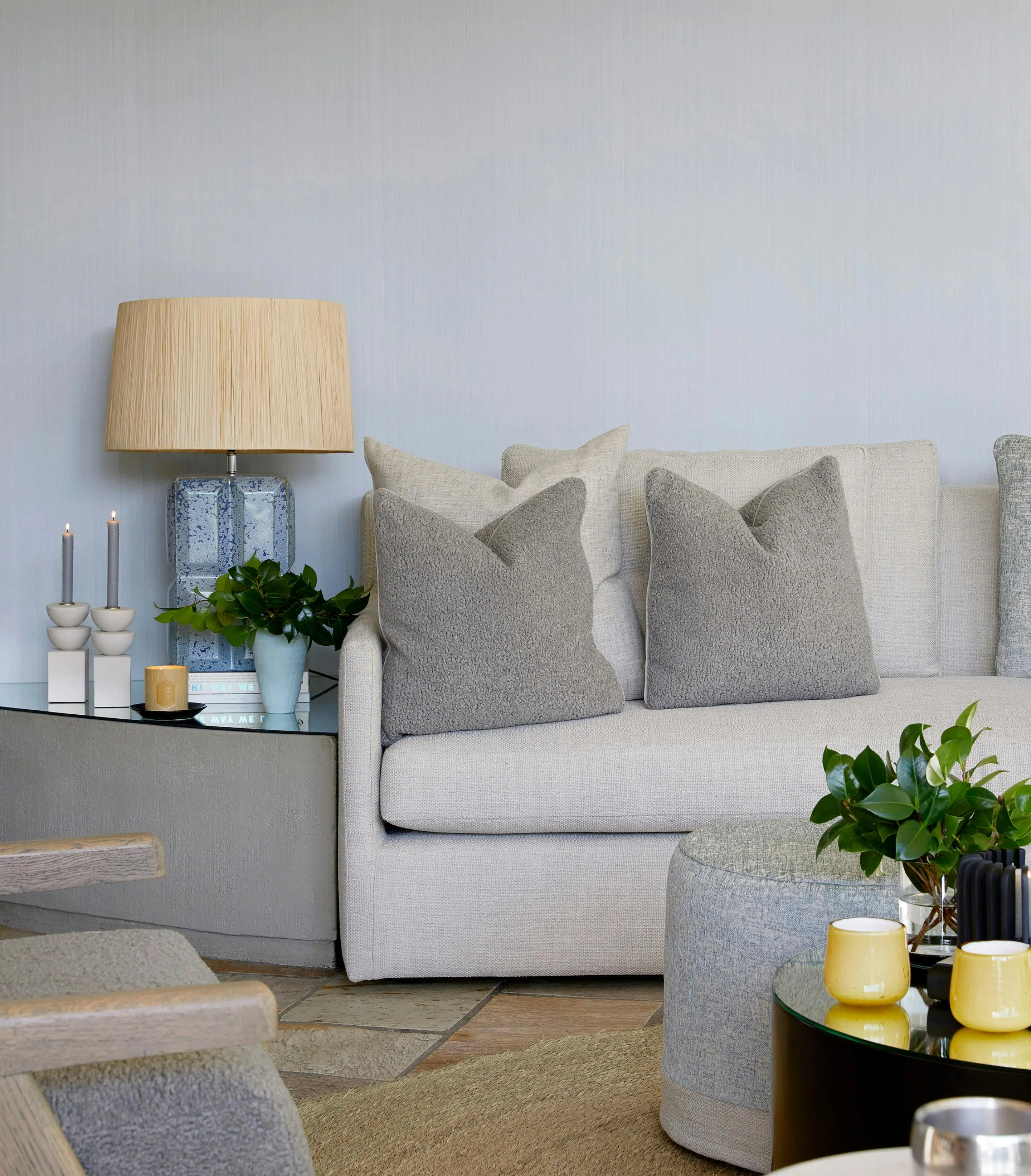 Close-up of a side table with a lamp and other decorative accents on top, next to a grey sofa.