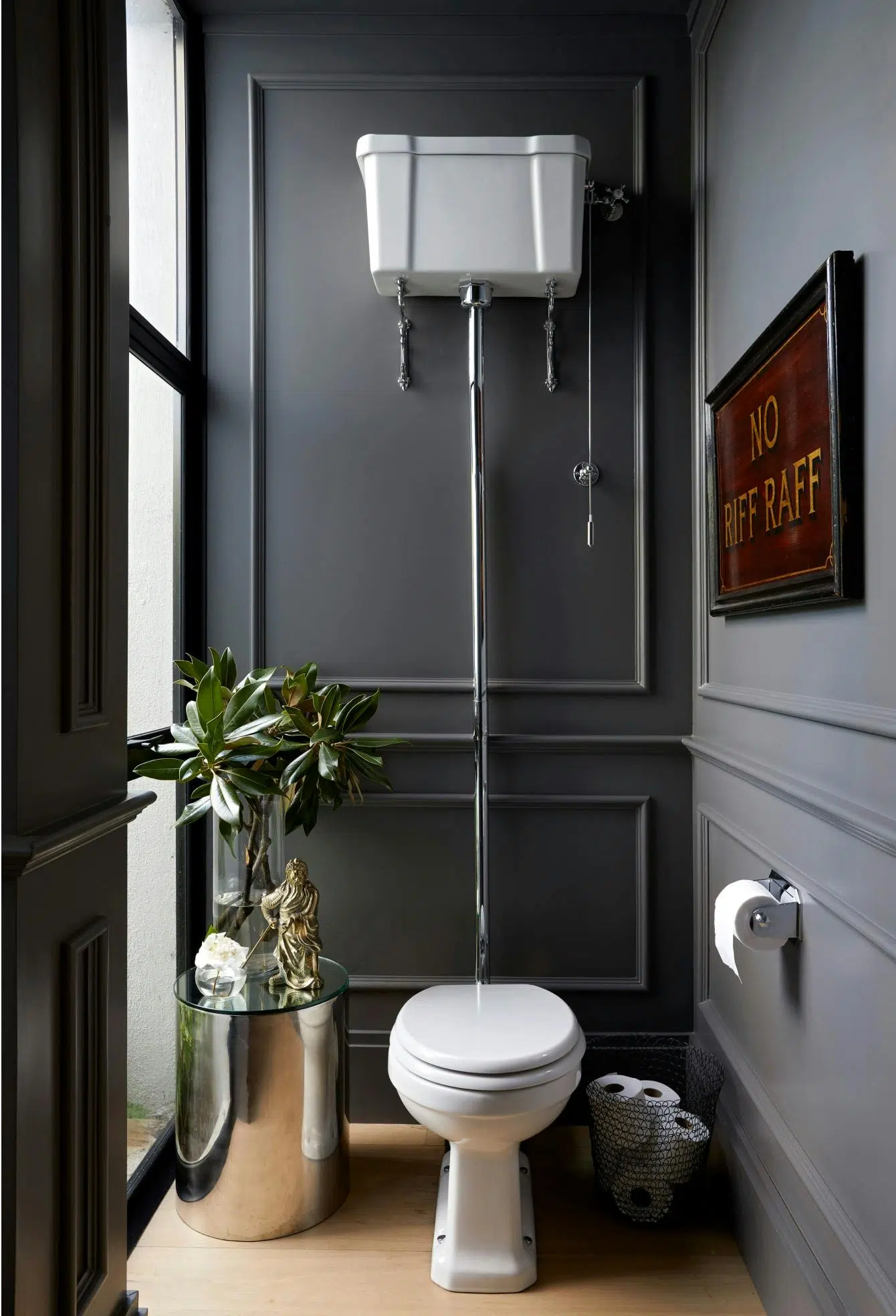 A bathroom with a toilet in the middle, a steel side table to left and a framed artwork on the wall to the right.