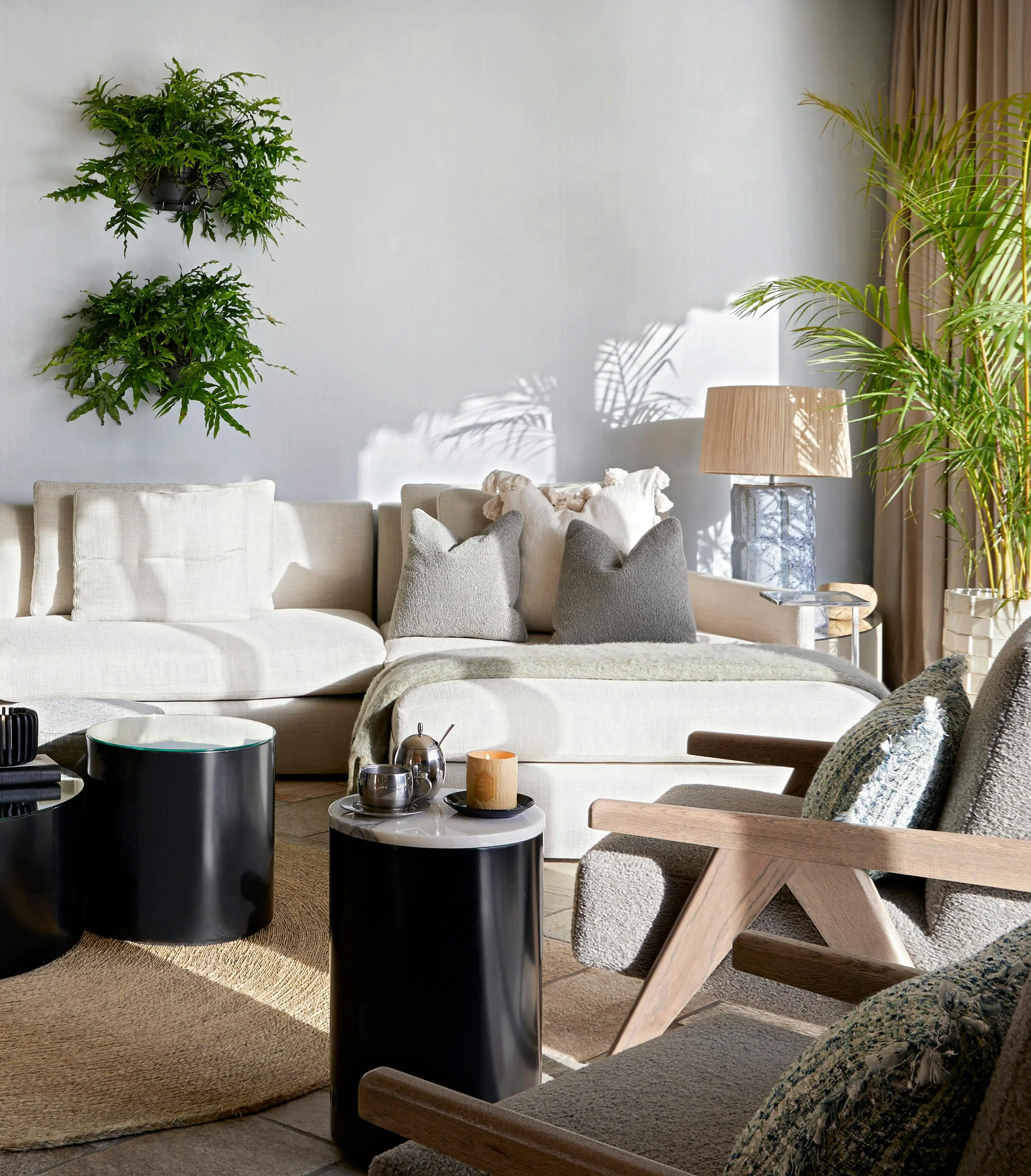 Close-up of a living room with natural light shining delicately on the walls, circular side tables are placed next to a contemporary chair with a curved sofa in the background.