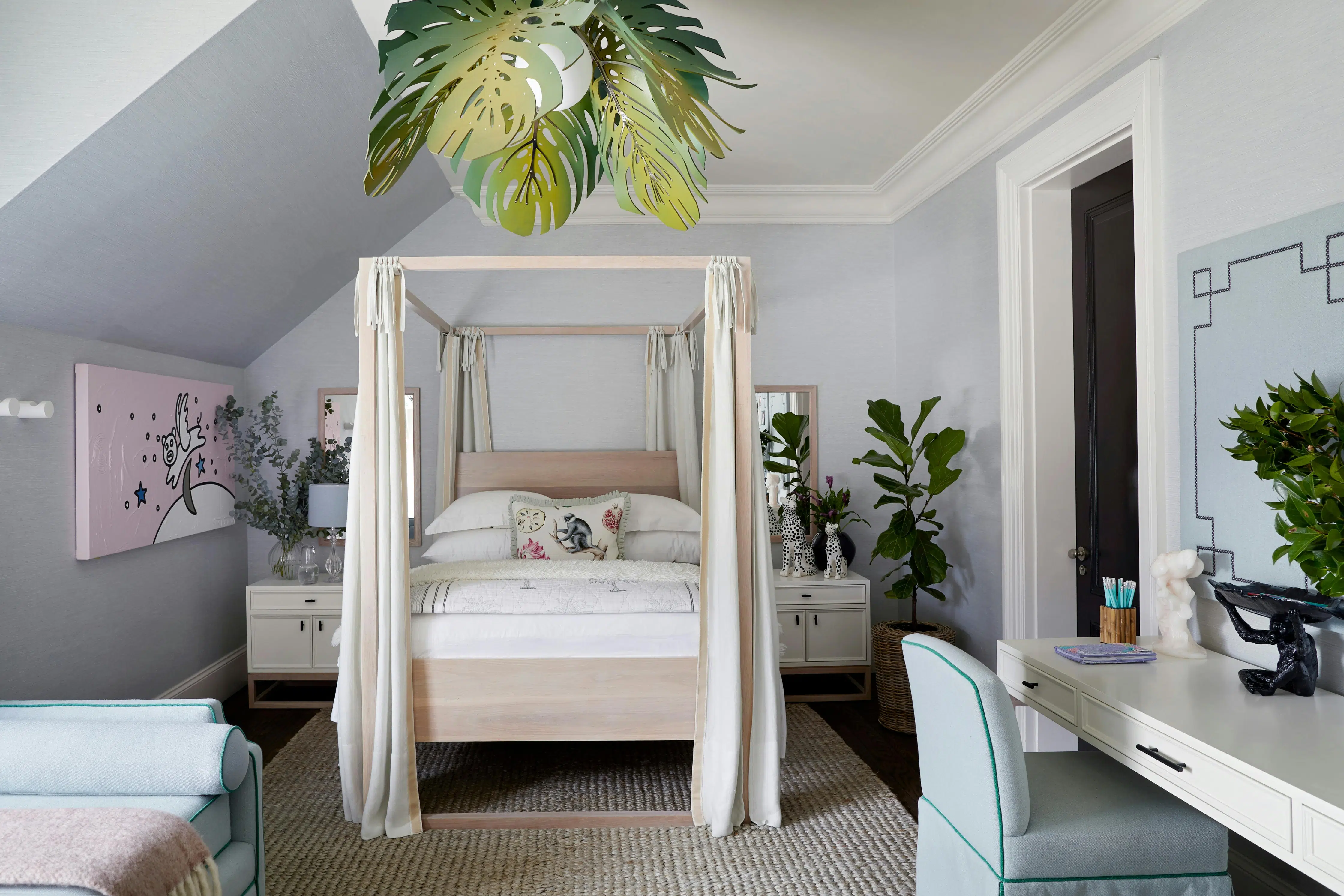 A modern children's bedroom with a 4-poster wooden bed, a desk to the right and pink artwork to the left.