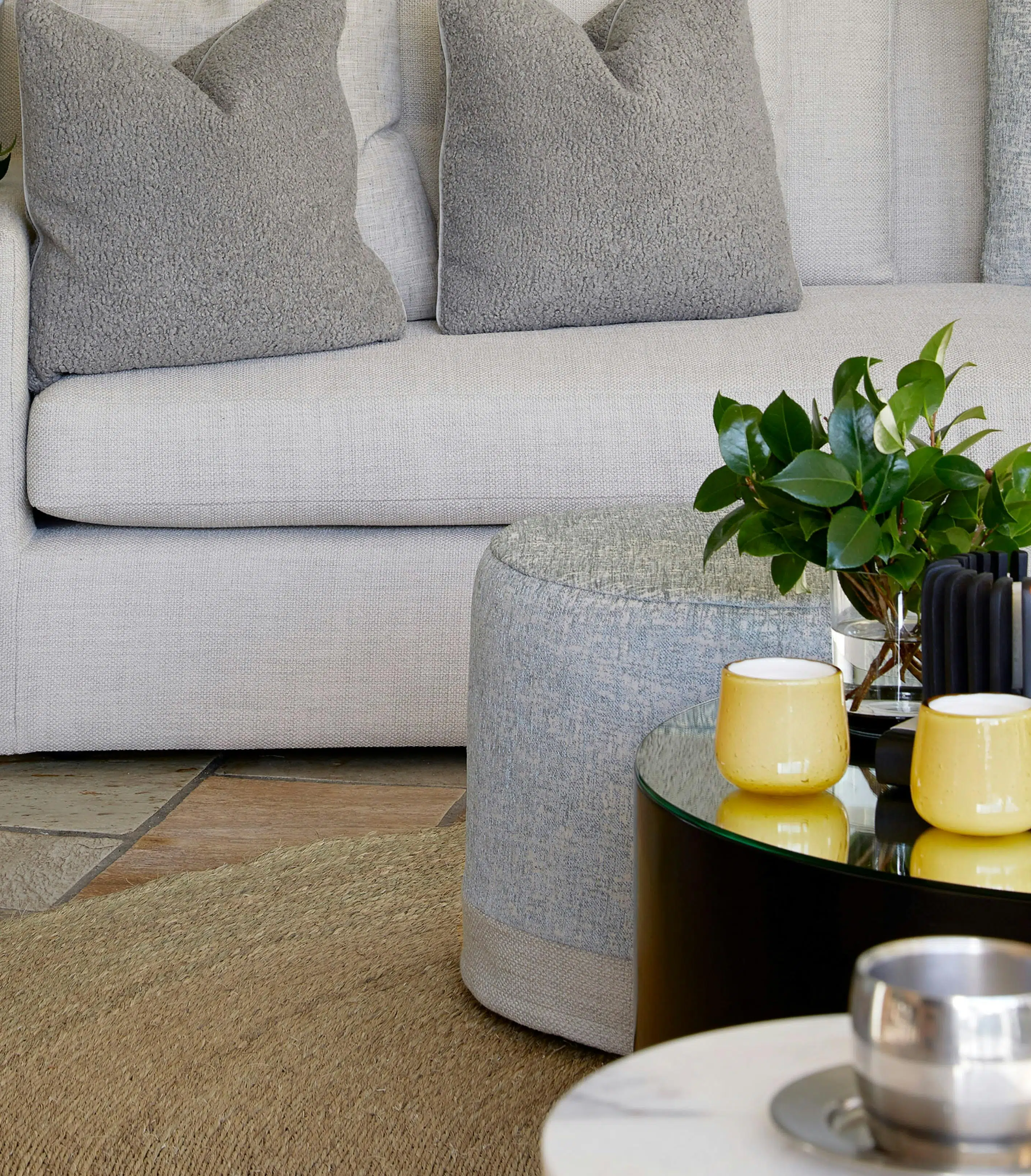 Close-up of a side table with a decorative accents on top, in the foreground with a modern grey sofa in the background.