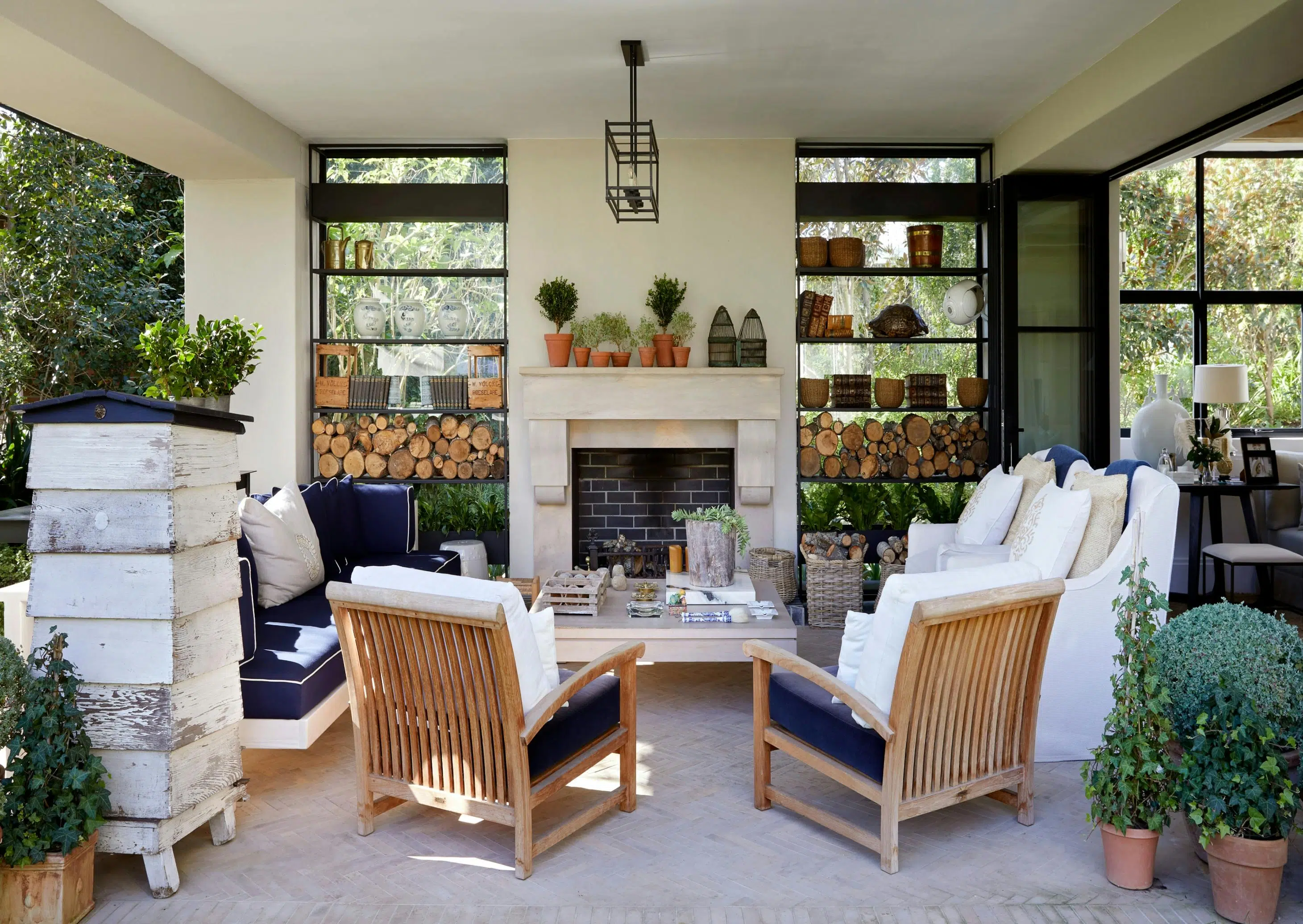 An outdoor entertainment area on a patio featuring wooden, slatted lounge chairs, a low coffee table and a fire place in the background.