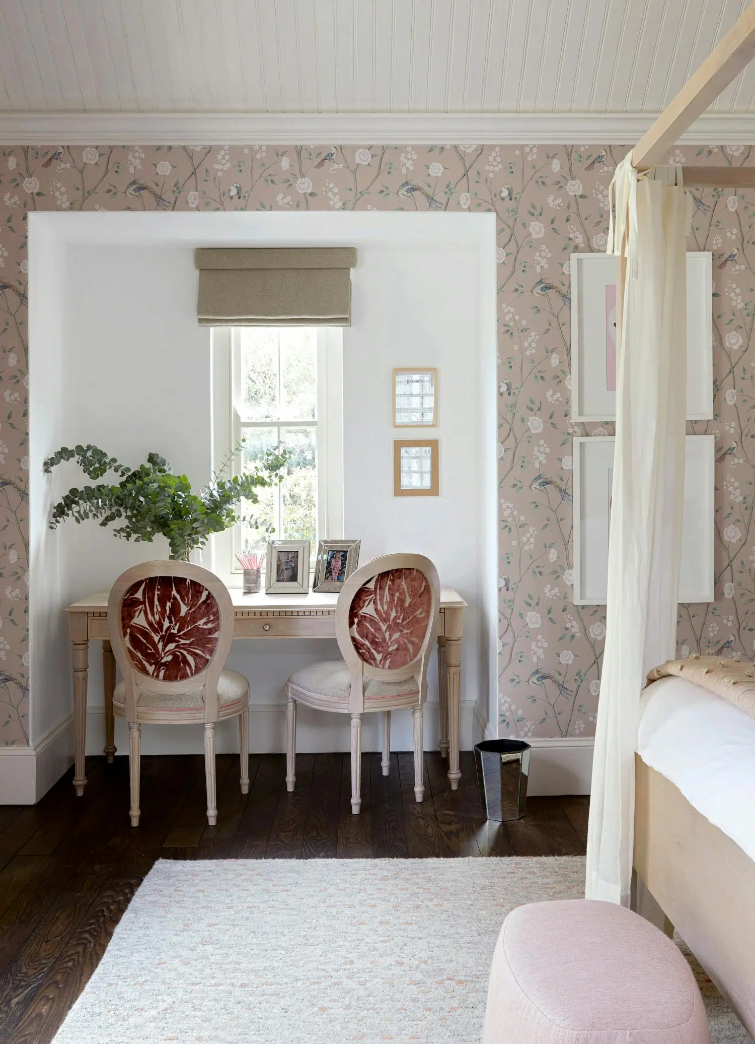 A bedroom with two chairs and desk in the centre of the image with the bed on the right.