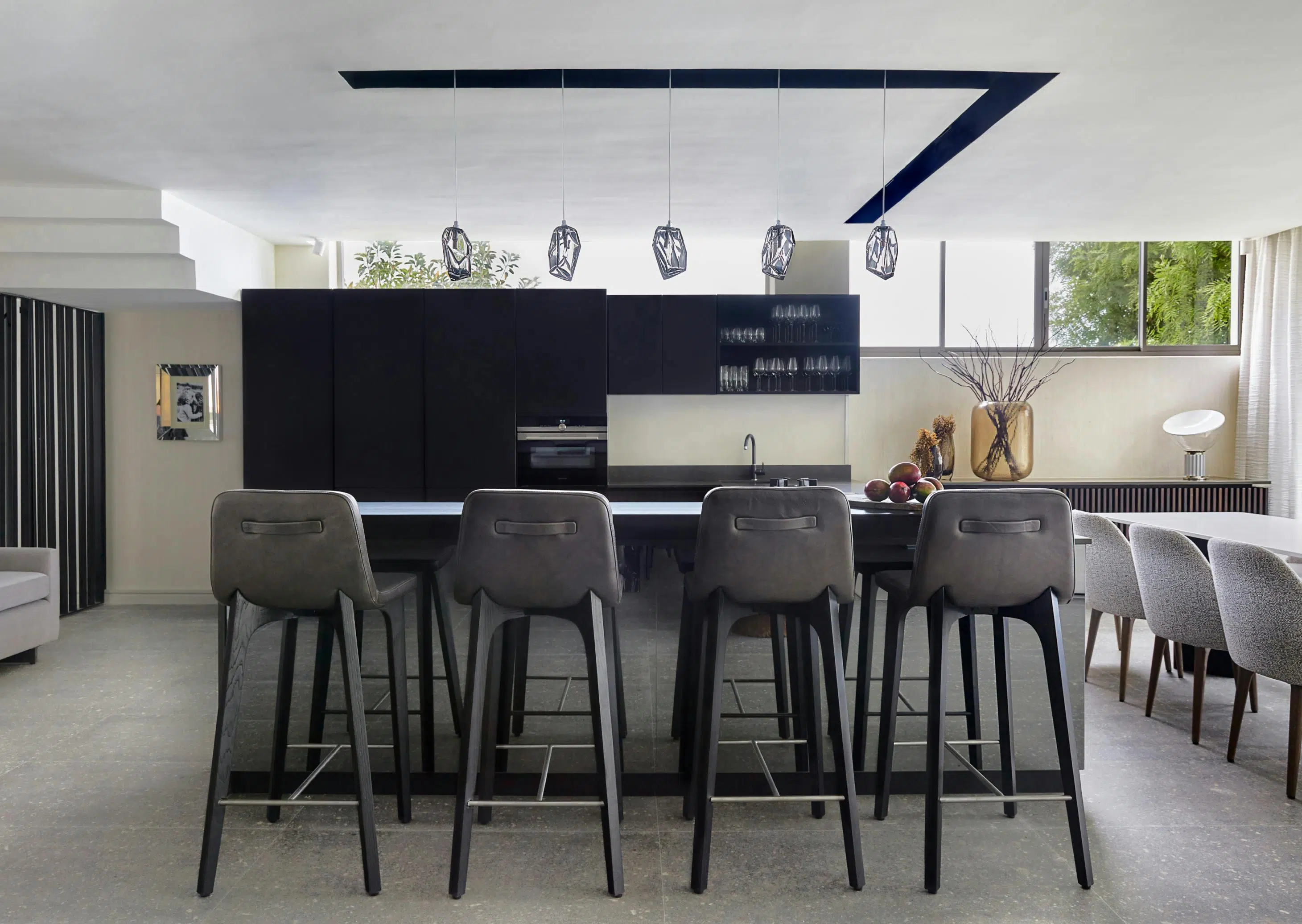 Four black barstools in the foreground with the kitchen in the background with a dining table and grey dining chairs to the right.