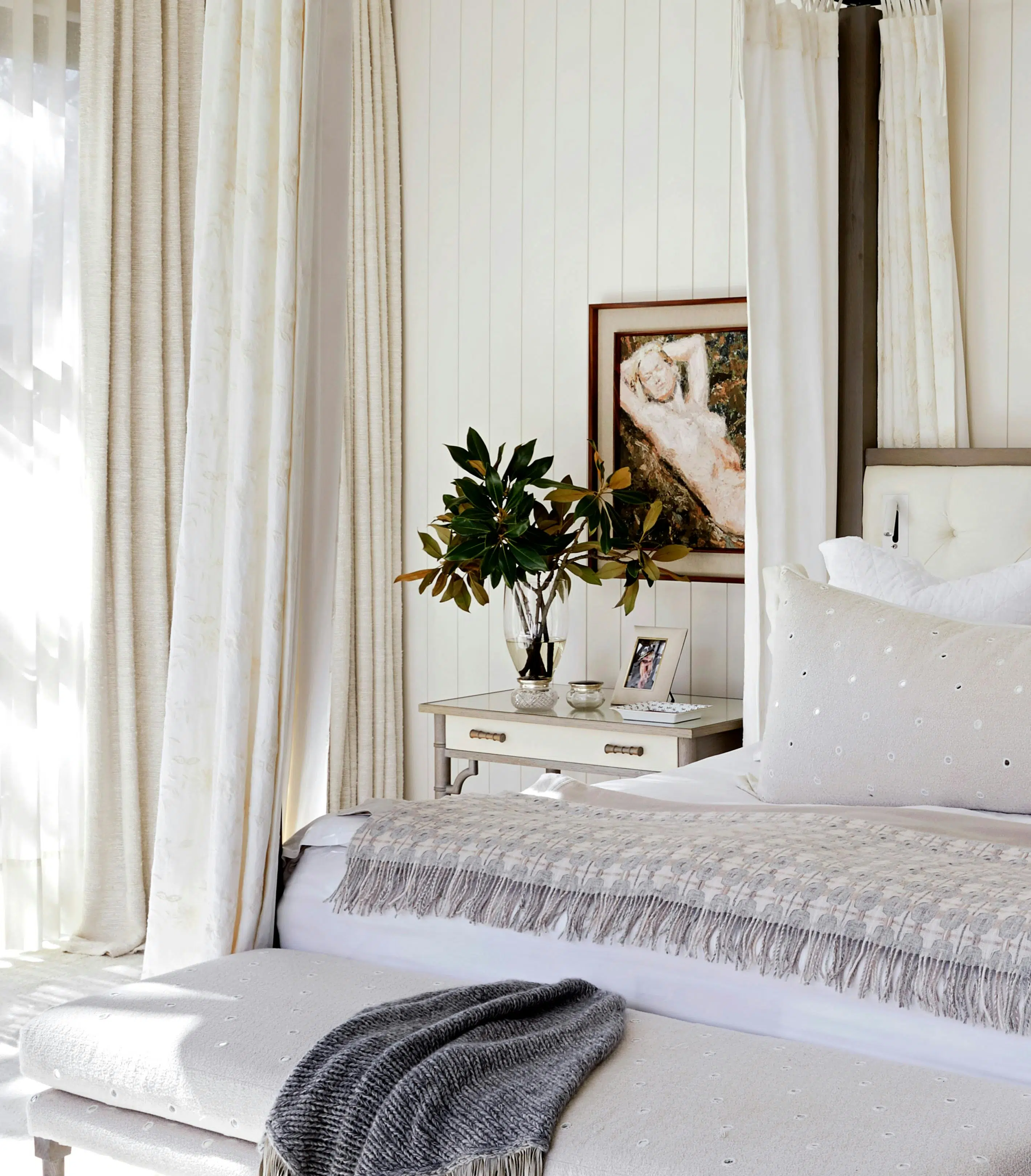 Close-up of a bedroom with a neutral colour palette. Artwork hangs just above a bedside that's placed next to a bed.
