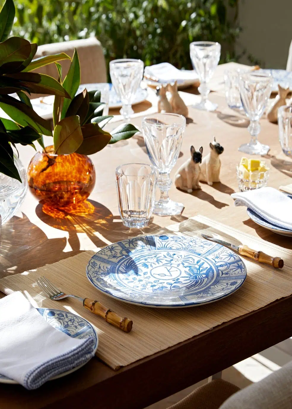 An outdoor, wooden dining table with crockery, cutlery and glassware on top.