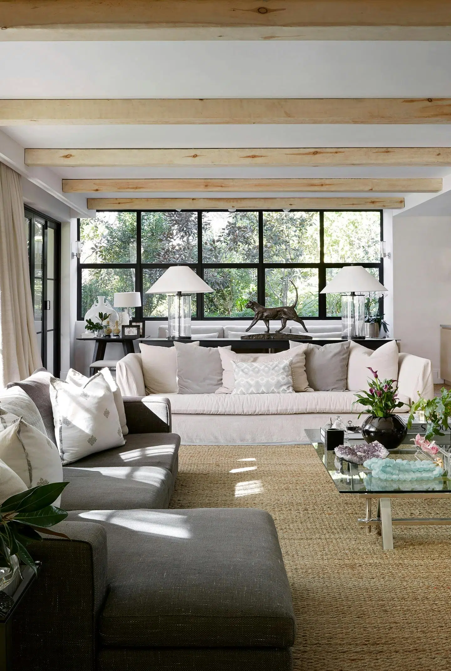 Close-up of a contemporary living room with one grey, and one white sofa with large windows in the background.