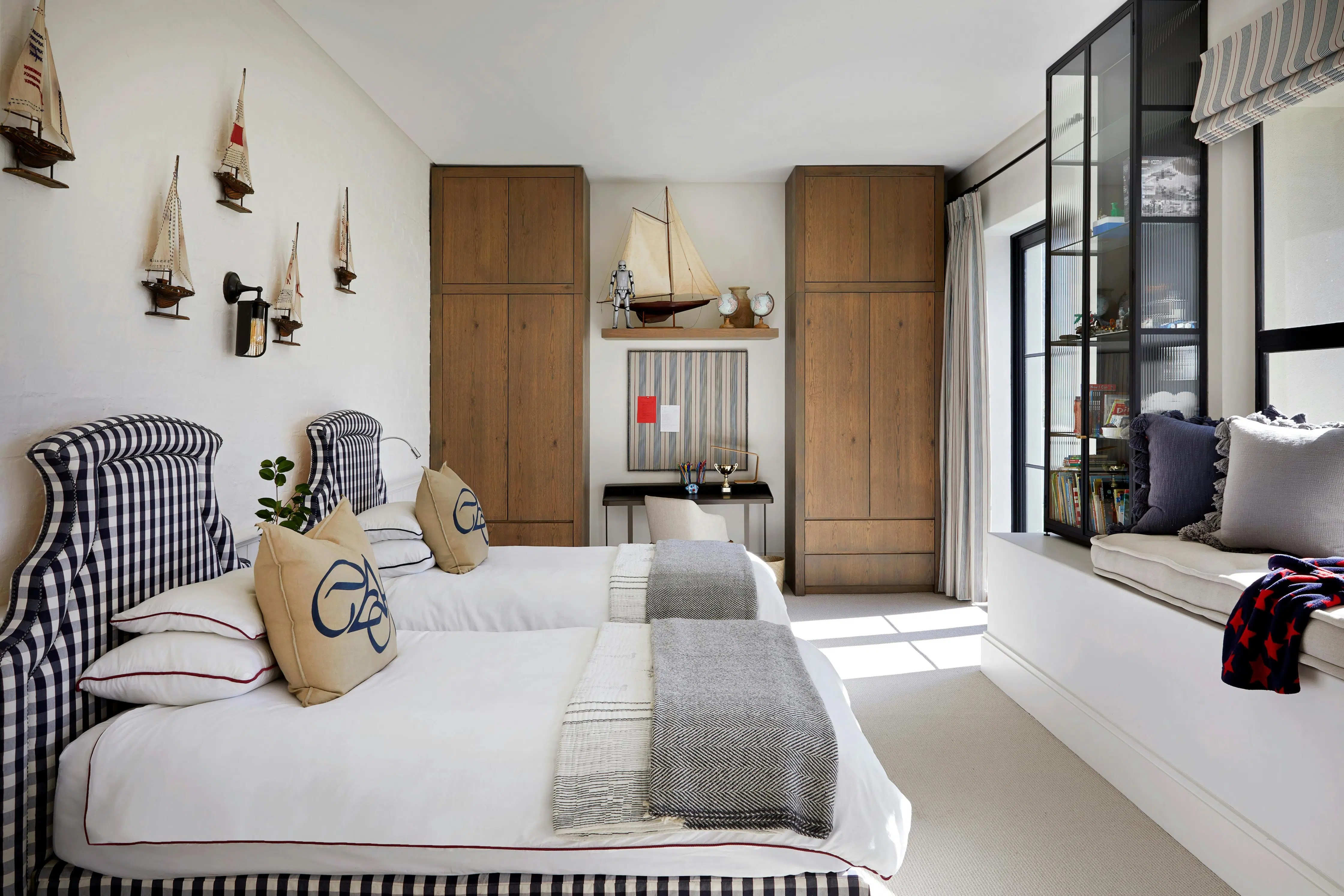 A nautical-themed bedroom with two single beds to the left, two wardrobes in the background and extra seating by the window to the right.