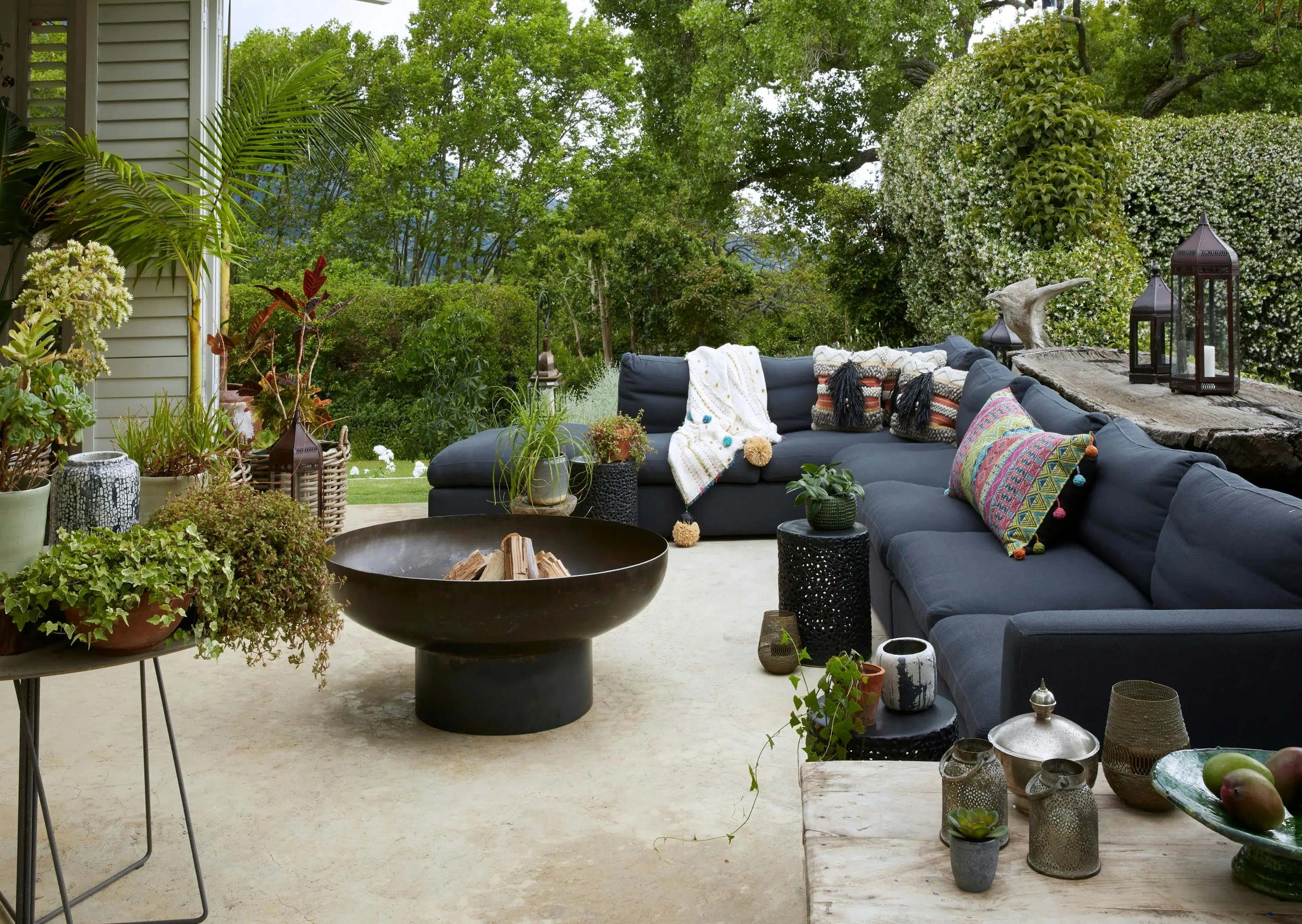 A Moroccan-inspired fire pit is surrounded by an outdoor sofa and lush greenery.